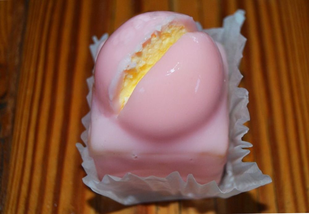 A small pink cake with a pink hemispherical dome on the top; the dome has a narrow wedge cut out of it revealing the cakey insides.