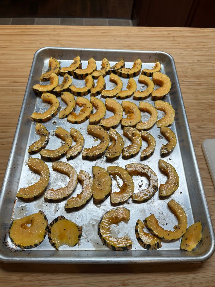 A cookie sheet filled with c-shaped slices of Delicata squash, brushed with melted butter and seasoned with salt and pepper. This is before putting them in the oven