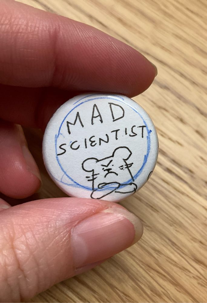 Hand holding a button that says “mad scientist “ with an angry mouse