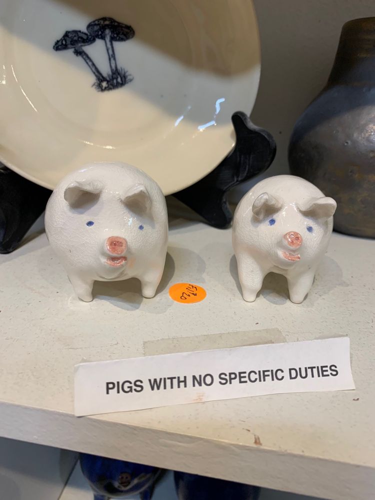 An image of two ceramic pigs labeled “pigs with no specific duties”