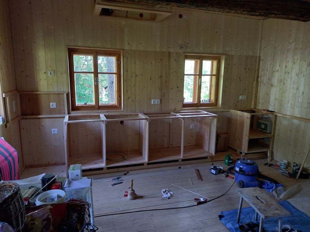 Küche in Aufbau. Alles aus Lärche.
Viel Werkzeuge liegt am Boden und ein Staubsauger. Viel Blau.