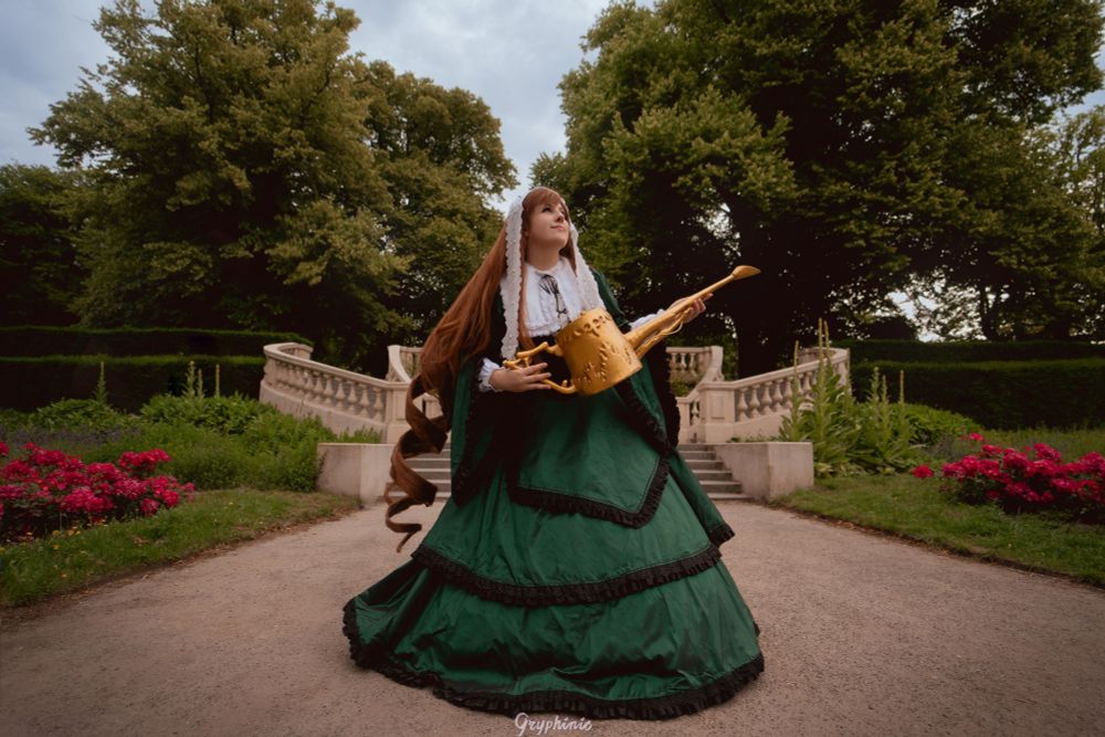Picture of me in my Suiseiseki Rozen Maiden Cosplay.
Big Green Gown with black and white details and holding a golden watering can. The biggest feature of this cosplay is the long wig with some big intertwined curles in the back. The wig takes up so much space it has its own name: Bertha.

Standing in the center of the road in front of some baroque style stairs in the garden of Landgoed Clingendael with the flowers and trees framing the picture.
