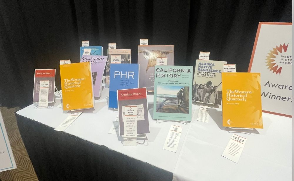 pic of award winning books and artciles at the WHA conference, with California History and a Fernandez painting of a woman mopping the sea at the border wall on the pacific