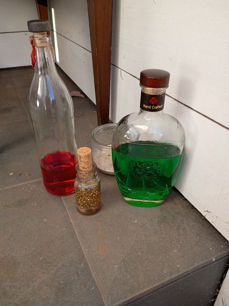 Three bottles containing 1) red liquid,2) green liquid & possible worms (ramen), al& gold glitter liquid. And candles.