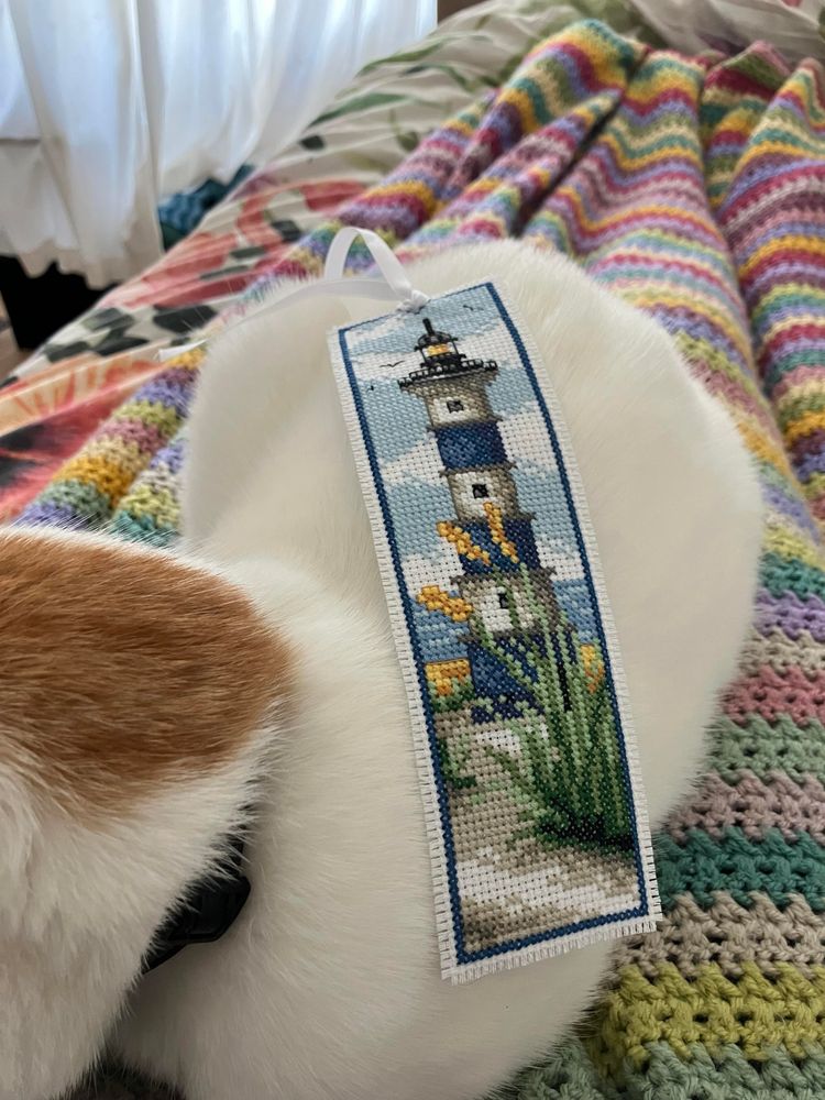 Boekenlegger met blauw-witte vuurtoren ligt op oranje-witte poes. Het borduurwerk is prachtig, met allemaal licht- en schaduwdetails en heel veel diepte in een heel klein plaatje 