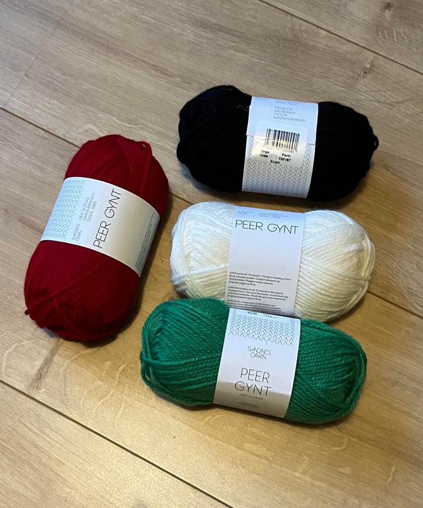 Vier bollen wol, links rood, daarnaast van boven naar beneden zwart, wit en groen 