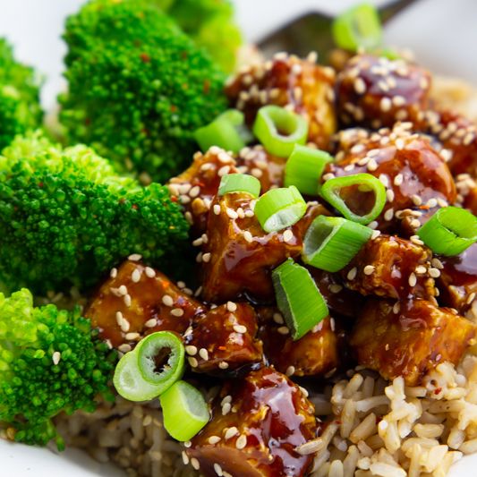 A bowl of rice with teriyaki tofu and broccoli with green onion and sesame.