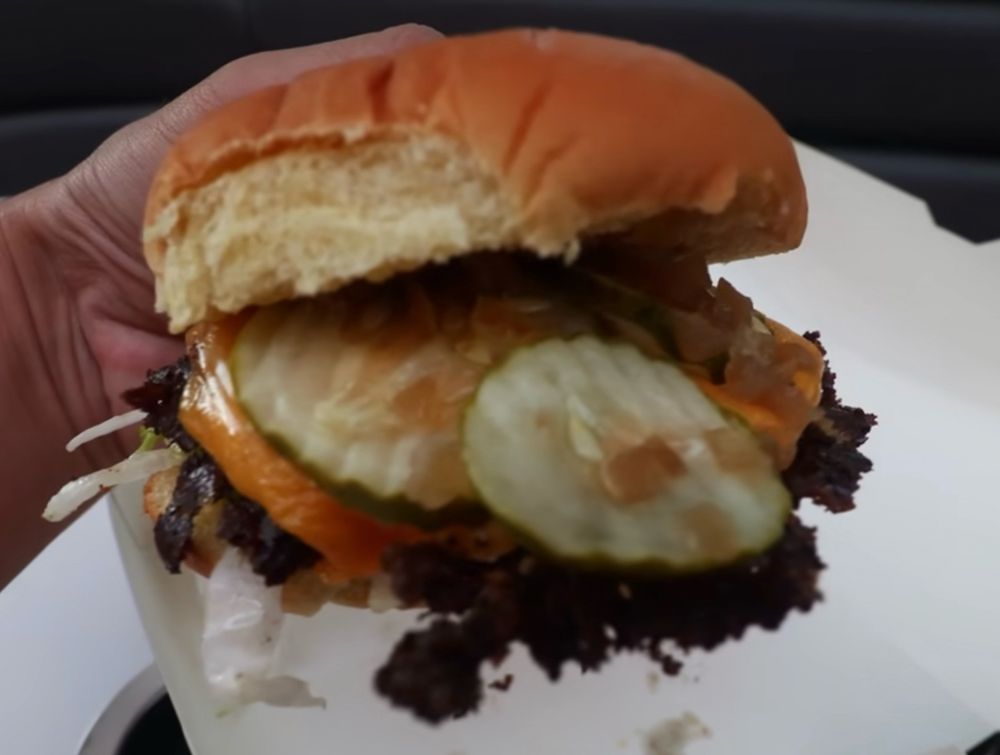 Untoasted buns try to keep a sloppy, burnt burger, wilted lettuce, and pickles wedged between them