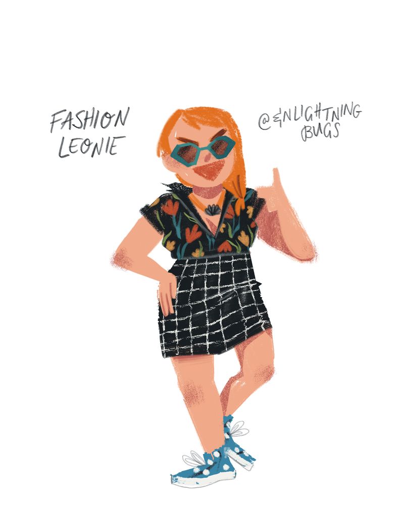Leonie in sunglasses, a black tropical shirt, a grid-print pencil skirt, and blue floral sneakers, giving a thumbs up
