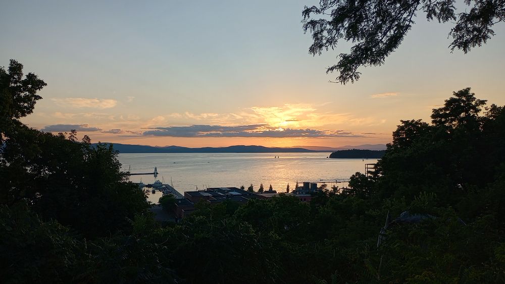 A view of Lake Champlain from Battery Park in the late evening with the setting Sun hidden behind a small band of clouds.