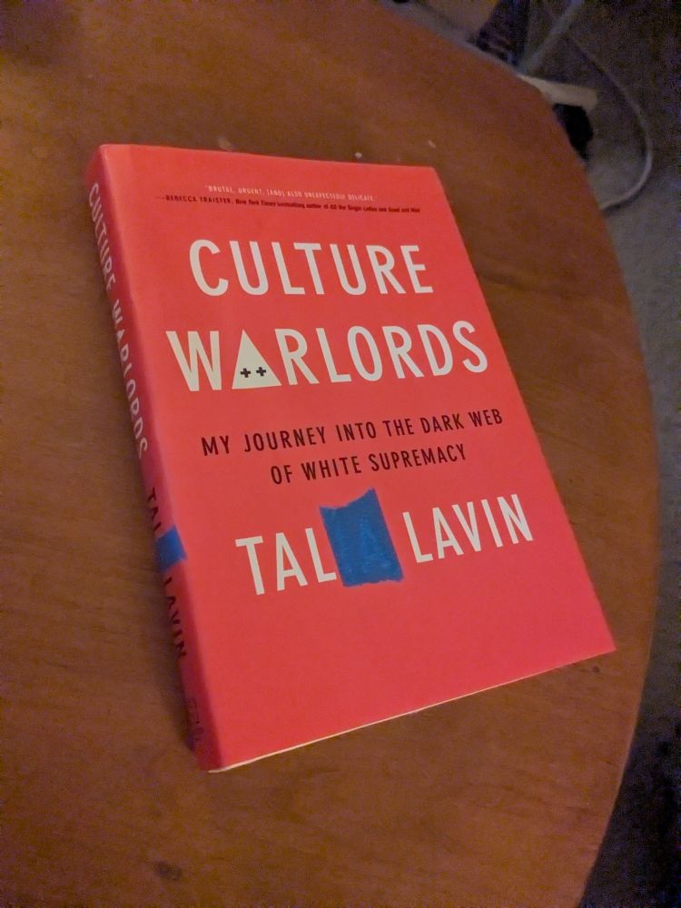 A pre-transition copy of Tal's book, Culture Warlords, sits on a scuffed wooden coffee table. The last two letters of his deadname as it appears on the front and spine of the dust jacket are covered with blue painter's tape.