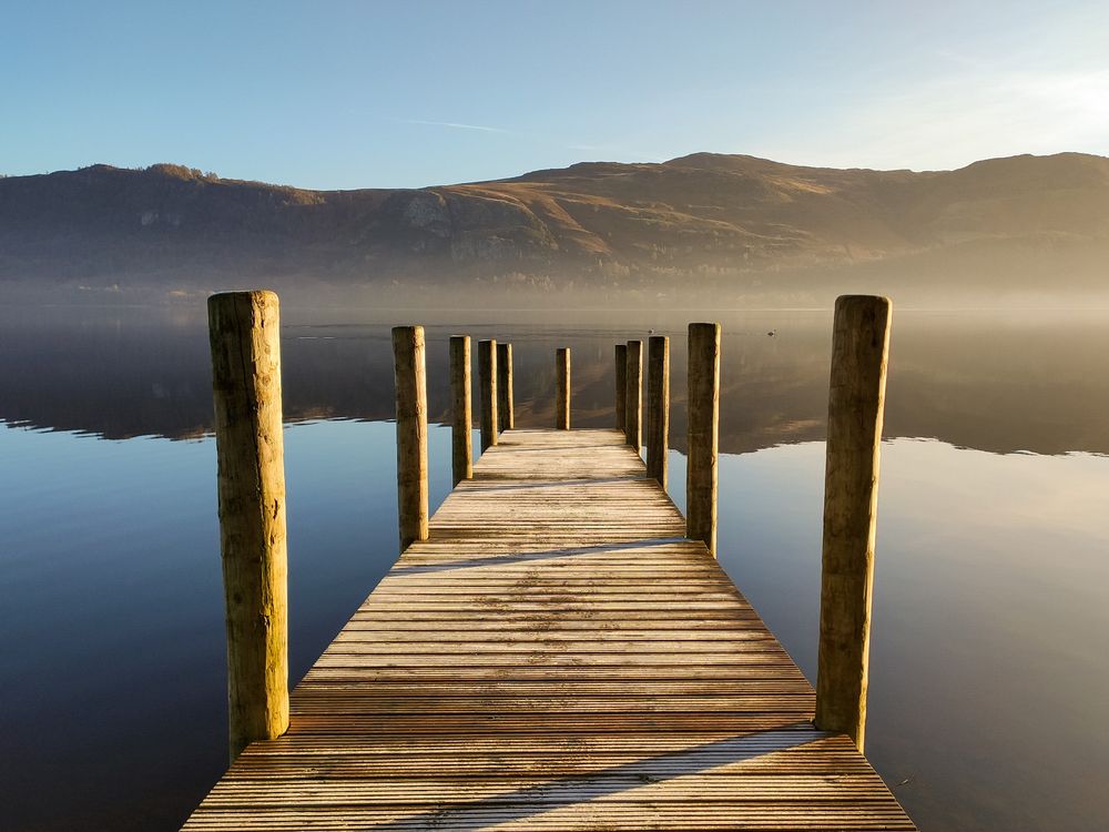 Woodem jetty sticking out with perspective into a reflective lake with mountains behind