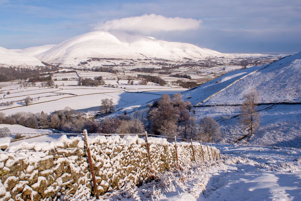 Snowy scene of mountain and valley with a dry stone wall leading across the foreground
