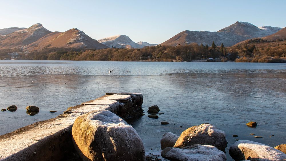 icy jetty leading out into lake with mountains behind