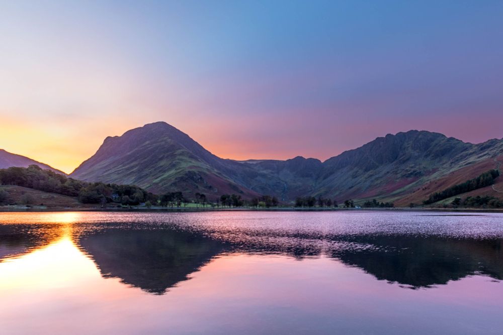Sunrise behind two mountsins with lake reflecting