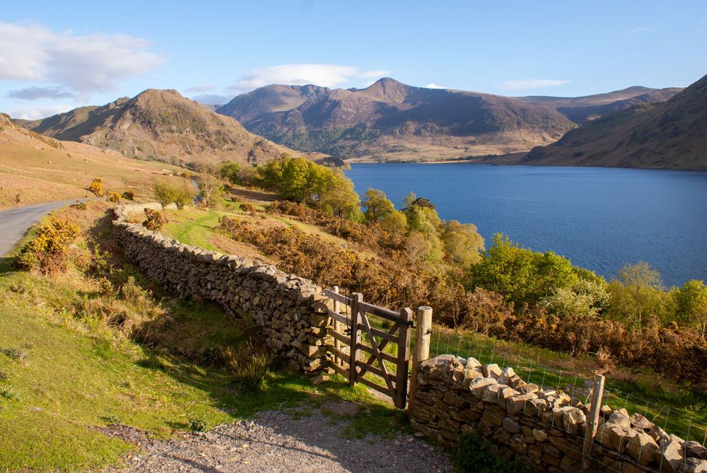 Gate and dry stone wall in front of lake with mountains behind