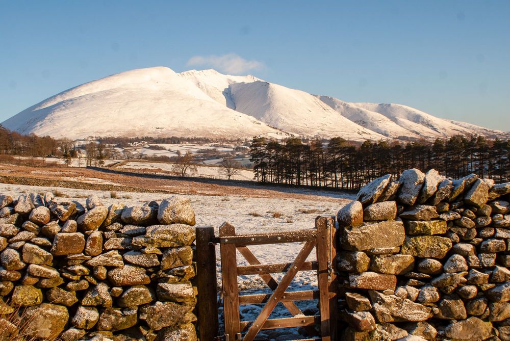 Snowy mountain with fry stone wall in front  A gate leads through