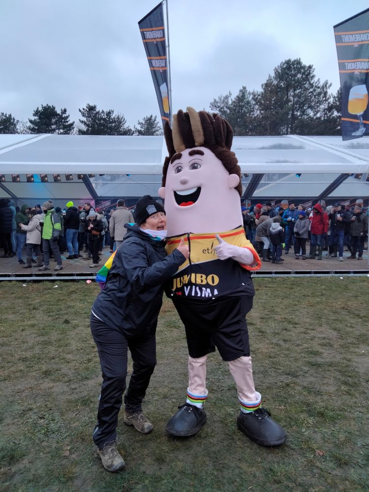 A Canadian woman in rain gear points at a giant Wout Van Aert in J-V kit. Wout's hair is bigger than ever.