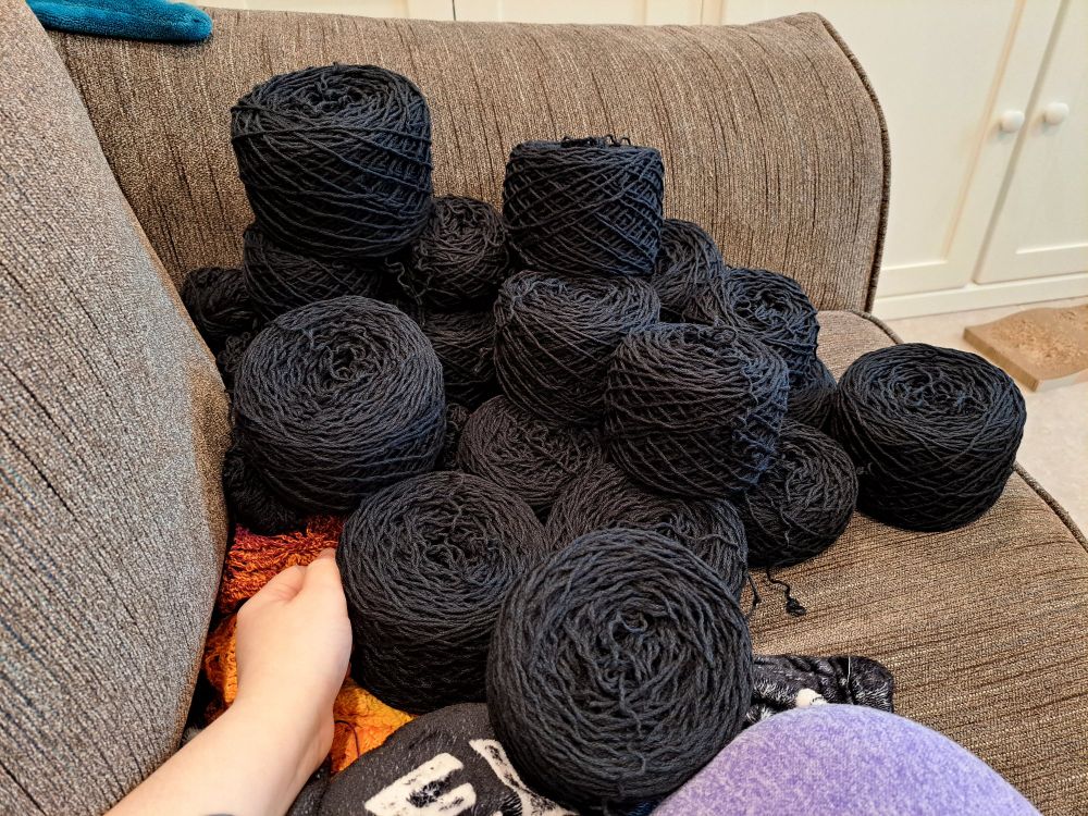 A pile of black yarn cakes on a couch. 