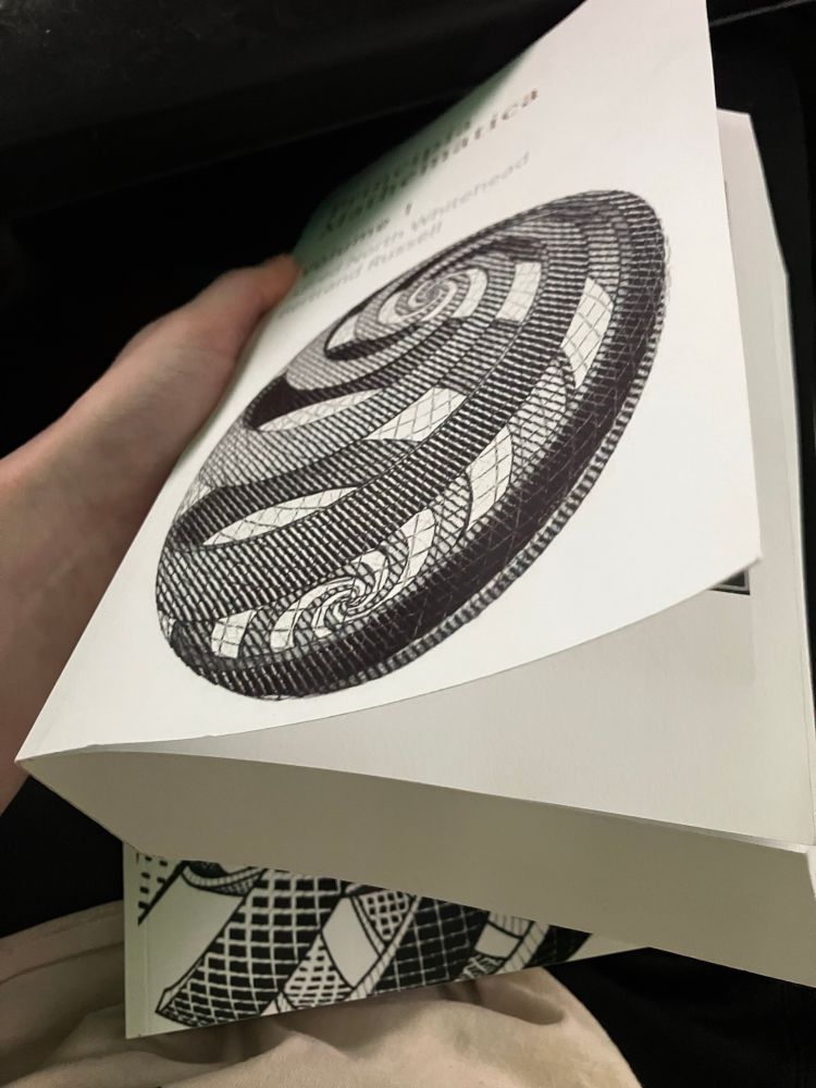 Blue holding one of two volumes of Principia Mathematica by Alfred North Whitehead and Bertrand Russell. 