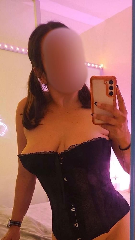 Liza in pigtails and a black corset in front of a mirror. Hazy pink lighting in the background.