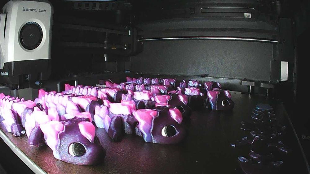 A plate full of purple dragons with pink scale accents and a pink gem shape on their foreheads, still on the plate of a 3D printer