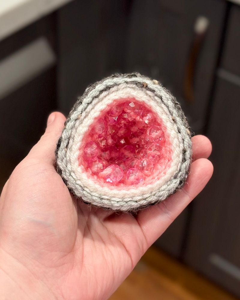 A soft crocheted geode made of yarn and pink beads on the inside to imitate crystals 