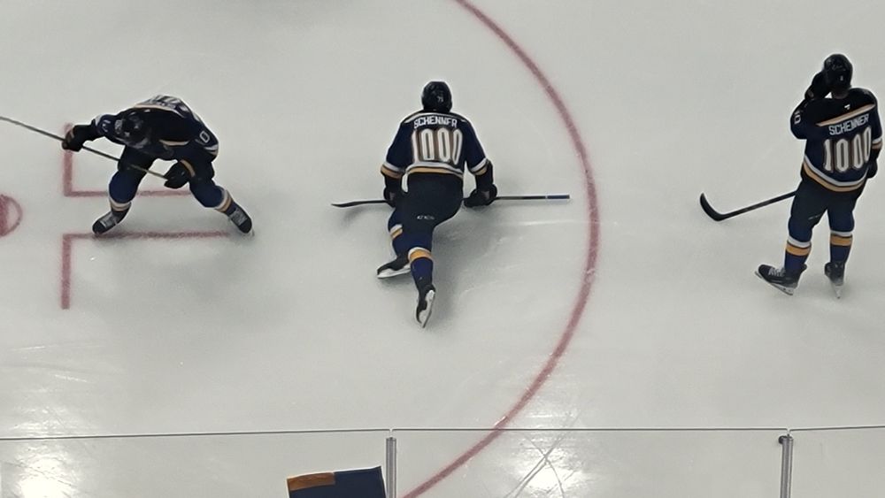Brayden's Schenn's teammates wearing Blues home Warmup sweaters with Schenner and the number 1000 on the back.