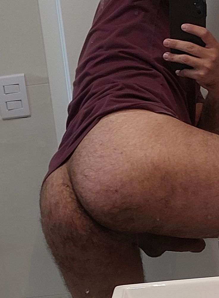De costas pra um espelho. A perna ligeiramente levantada mostrando a bunda e o pau. 