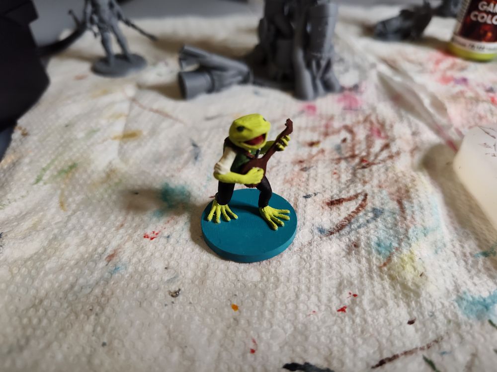 A Bullywug Bard plays a lute and sings a song about rainbows