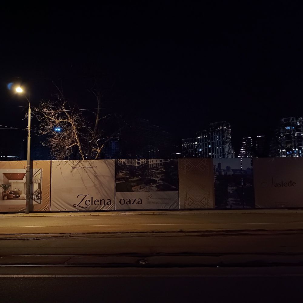 Construction site in Belgrade, in the foreground the posters of the future buildings, in the background a series of tall building lit at night
