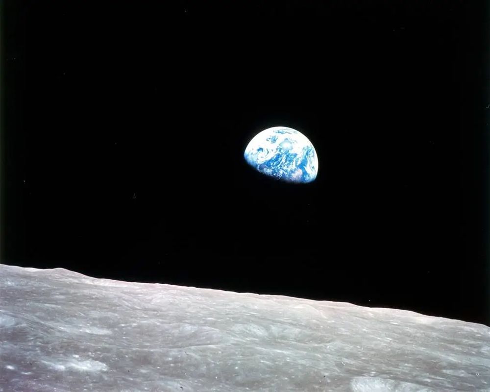Photo of the planet Earth taken from Apollo 8 during the lunar sunrise. You can see the Moon and its grey, pockmarked surface curving in the foreground and a portion of the planet Earth emerging from the darkness of space in the background like a distant, precious blue and white gem.