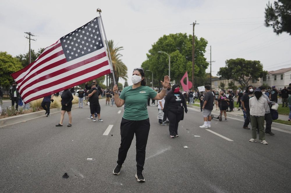 Protester wearing a green shirt and white N95 mask holds an American flag