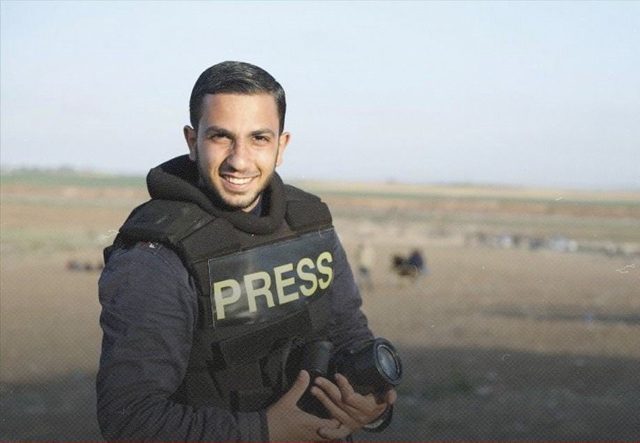 Photo of a young, handsome smiling man with dark hair wearing a PRESS vest