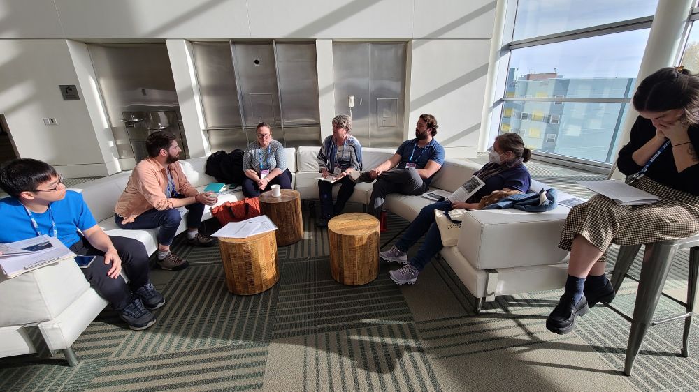 Workshop attendees sit on white couches as they talk about citizen and community science case studies
