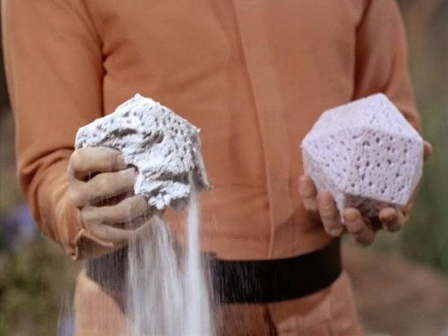 Rojan holds two porous cuboctahedron solids. He is crushing one of them, killing an Enterprise crew member.