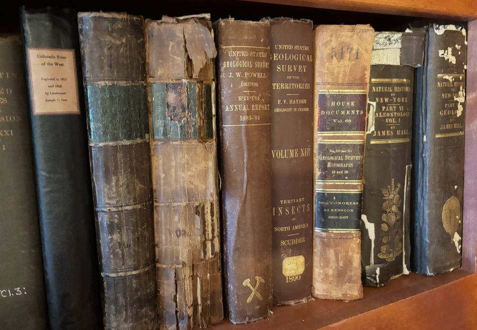 A bookshelf filled with a bunch of old looking books, including many Geological Survey titles. 