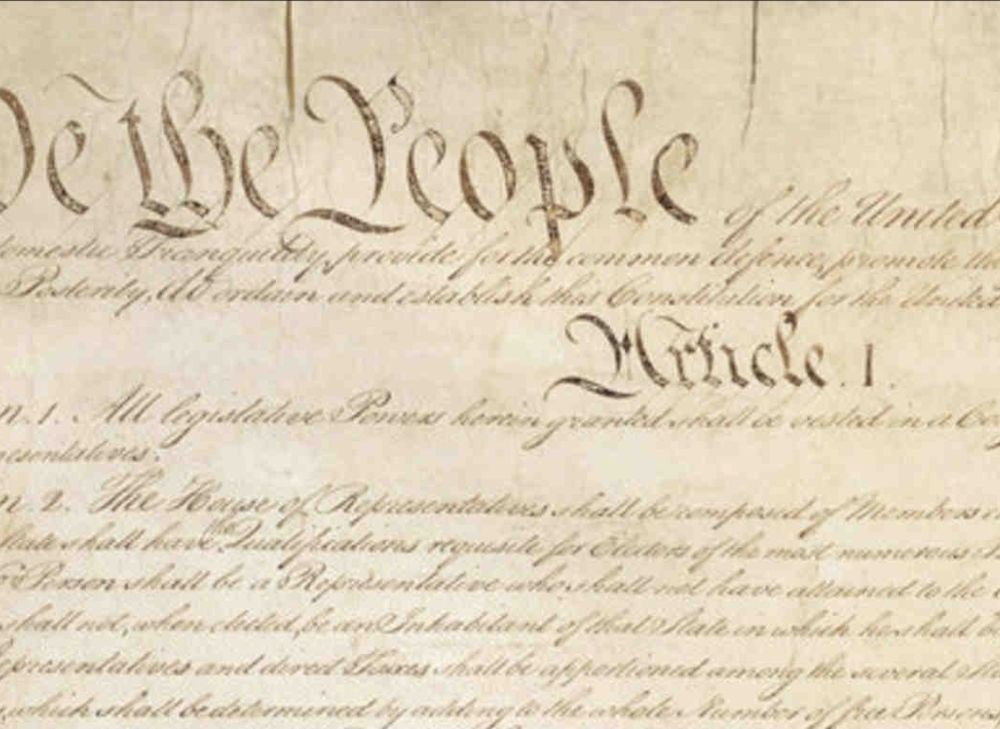 A faded image of the US Constitution with "We The People" and "Article 1" visible in large calligraphy 