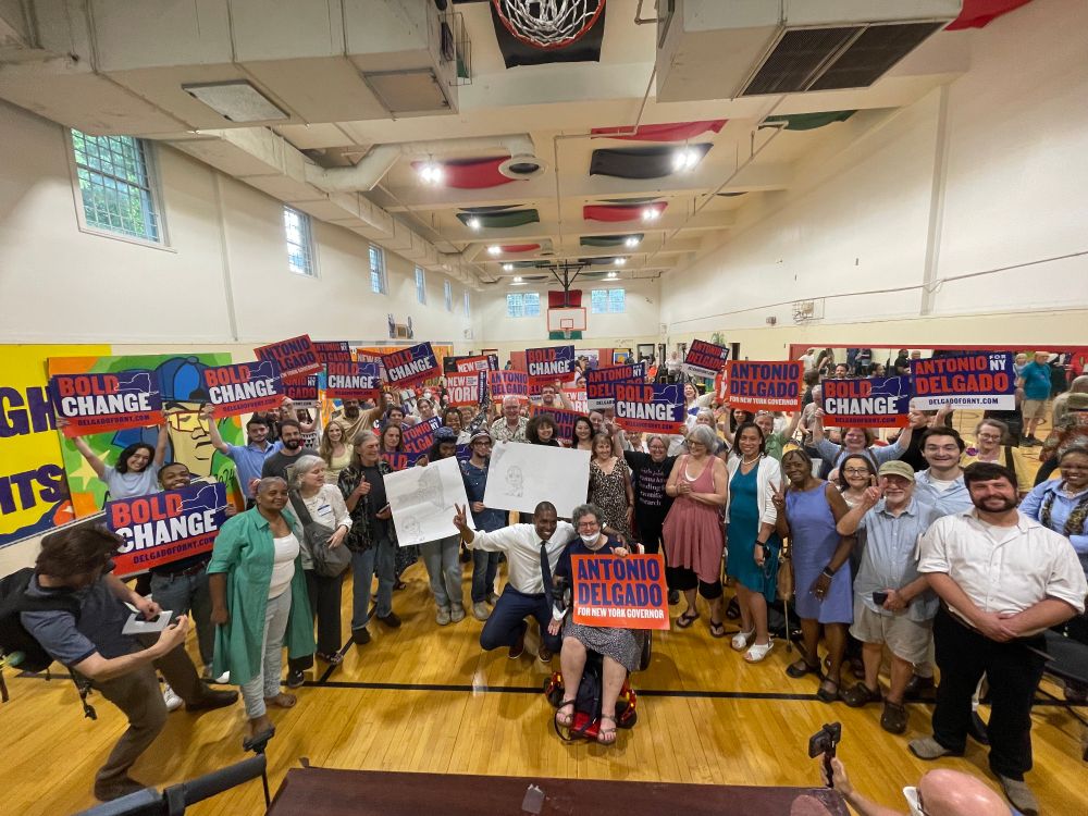 A crowded gymnasium of people holding up signs for Antonio Delgado, with Mr. Delgado himself in the center.