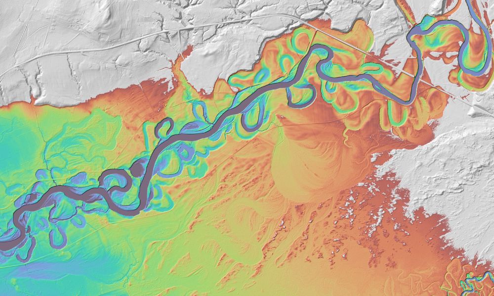 Dark blue river channel runs diagonally across image. Brightly colored landscape shows topography around creek. 