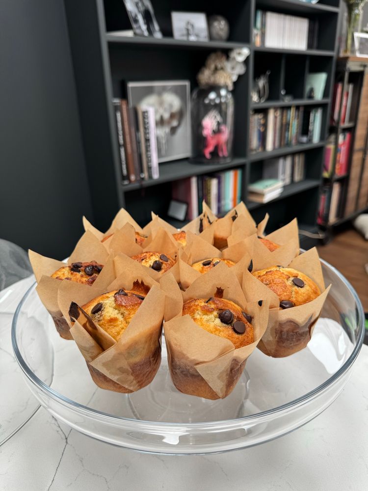 An arrangement of chocolate chip muffins on the base of a glass cloche, the background shows a large built in bookcase painted black