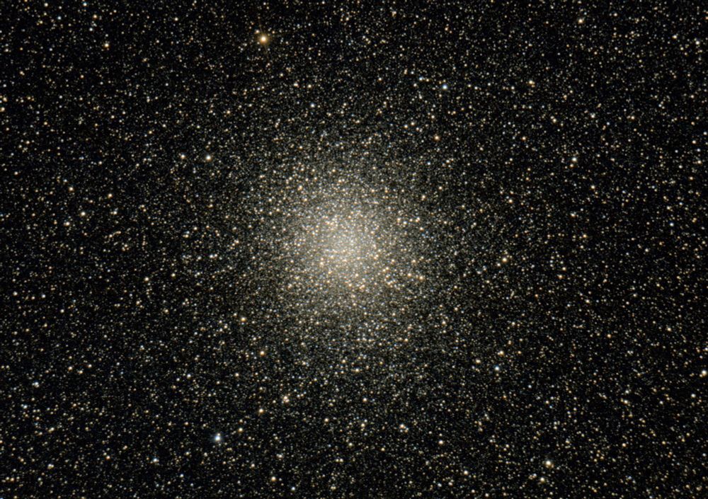 Messier 22, the Great Globular Cluster in Sagittarius, a roundish mass of stars, dense and bright in the middle, surrounded by countless other stars in the foreground.