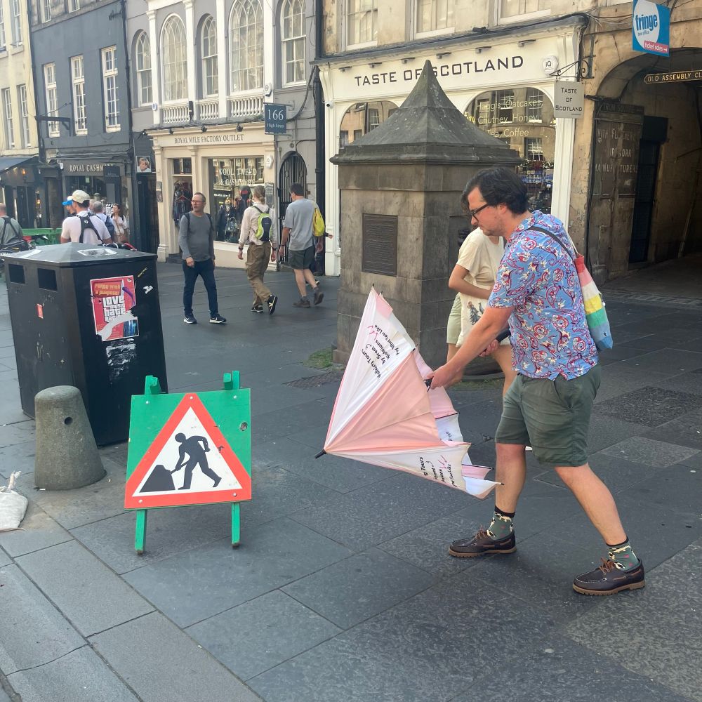A picture of a man opening umbrella next to a Men at Work street sign, creating a humorous effect