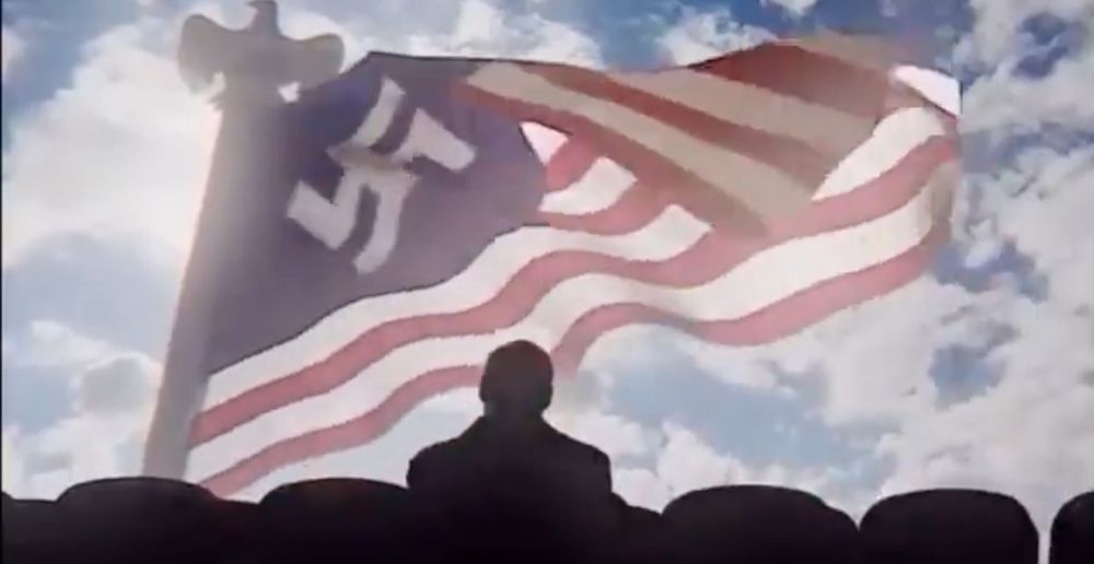 Still from Amazon’s adaptation of Philip K Dick’s ‘The Man in the High Castle’ where a character sits in a theater while an ‘American’ flag (with a swastika instead of the 50 stars) waves on the screen. 