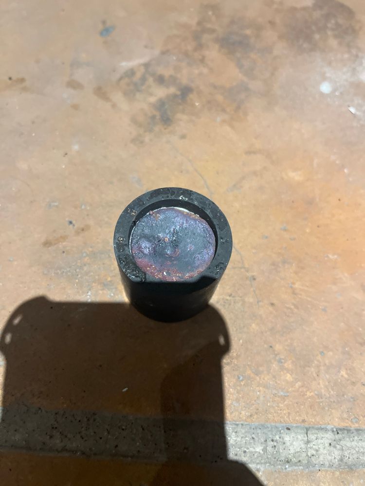 A graphite crucible full of a rather grey looking metal, it has a purple sheen to it