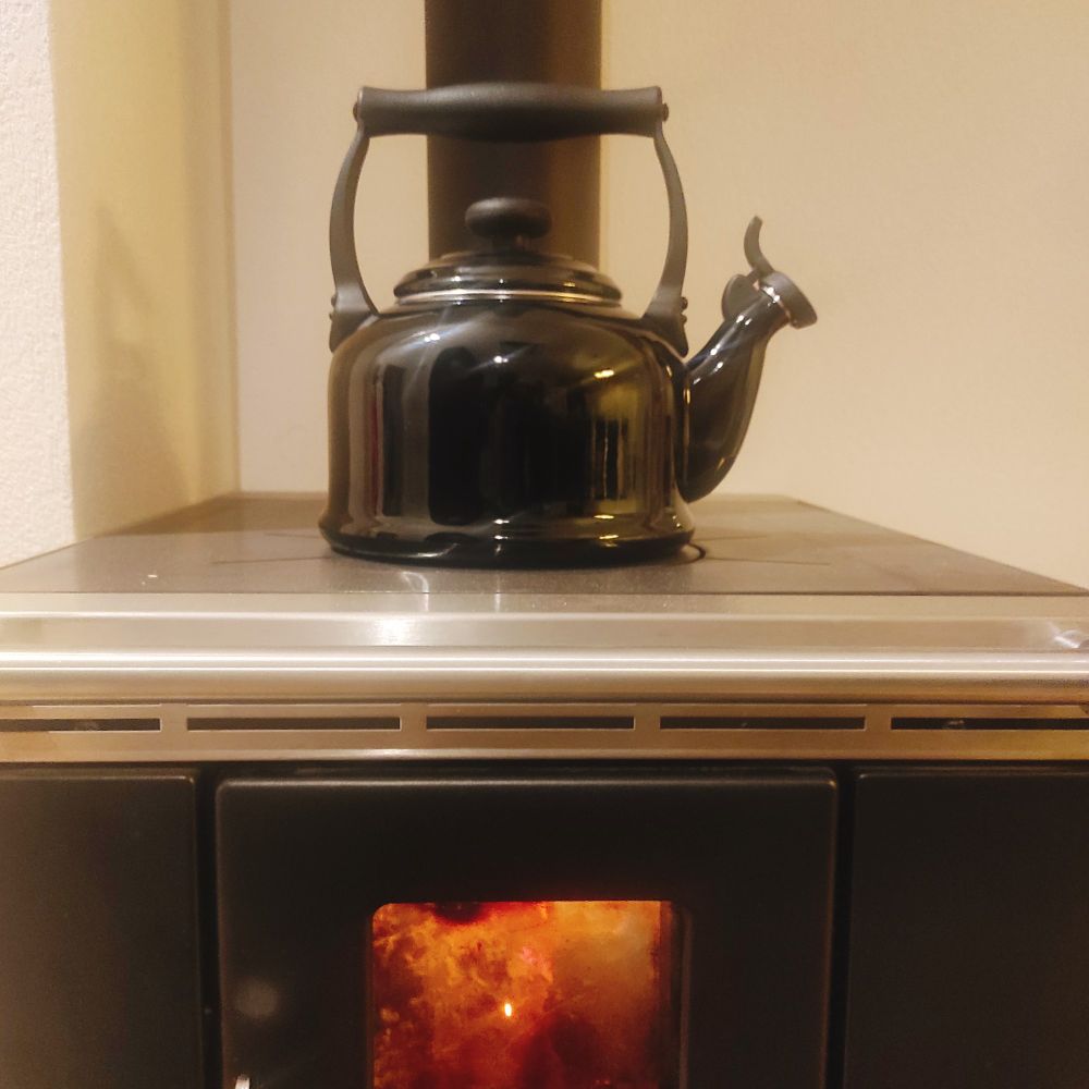 Schwarzer Wasserkessel steht auf Feuerherd. 