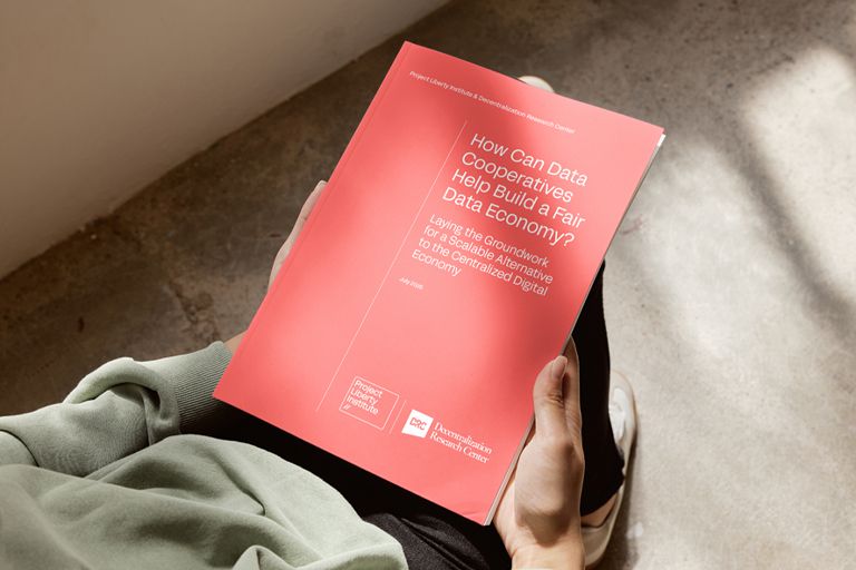 Photograph of someone holding a new report from Project Liberty Institute and the Decentralization Research Center titled "How Can Data Cooperatives Help Build a Fair Data Economy?" 