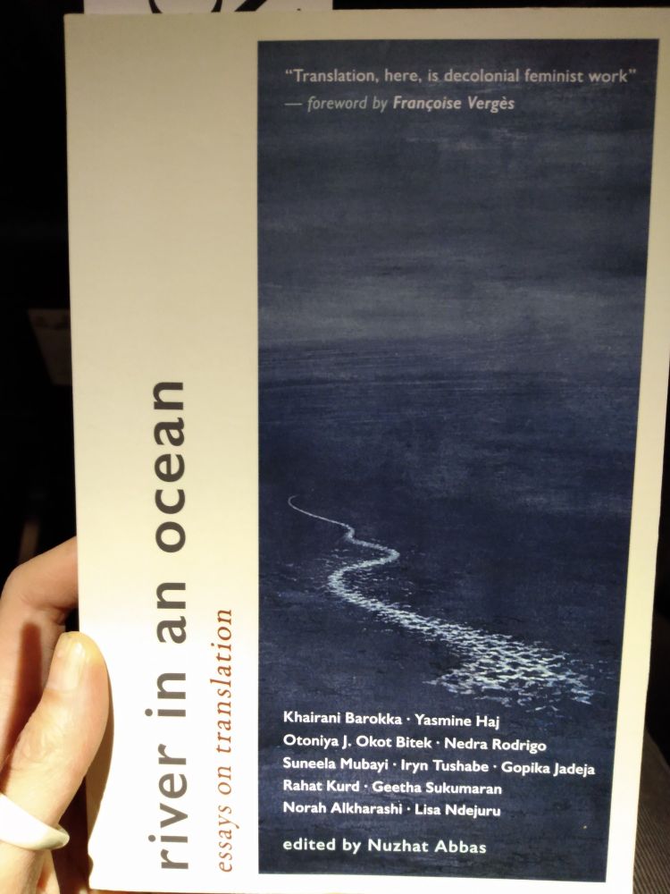 Cover of 'river in an ocean: essays on translation' has an image of a dark blue ocean with a winding white wake in it, names the editor Nuzhat Abbas and the authors Khairani Barokka, Yasmine Haj, Otoniya J. Okot Bitek, Nedra Rodrigo, Suneela Mubayi, Iryn Tushabe, Gopika Jadeja, Rahat Kurd, Geetha Sukumaran, Norah Alkharashi, Lisa Ndejuru.
