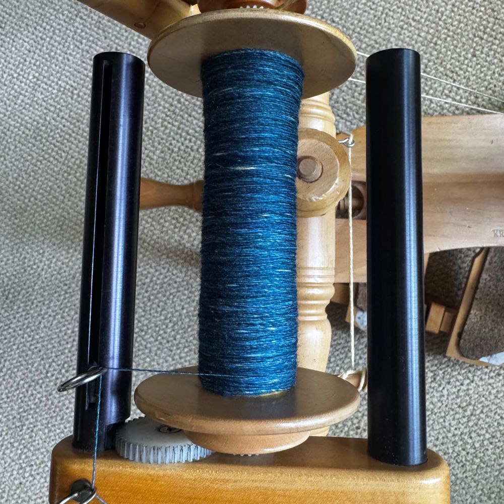 A spinning project in progress. It is a single spun fairly finely on a wooden WooLee Winder bobbin. The current color is blue, but some bits of yellow are poking through underneath. 