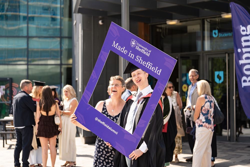 A person in a cap and gown poses with a family member holding a purple selfie frame with the words ‘Made in Sheffield’